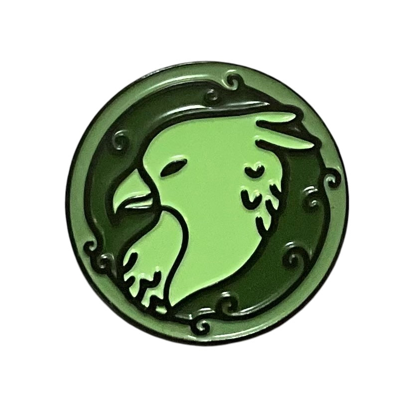 A green enamel pin shaped like a griffin head with decorative details around the edge.