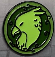 A green enamel pin shaped like a griffin head with decorative details around the edge.