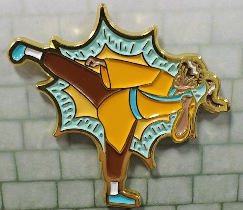 An enamel pin featuring a Monk character in yellow and blue colors with a golden ki outline.