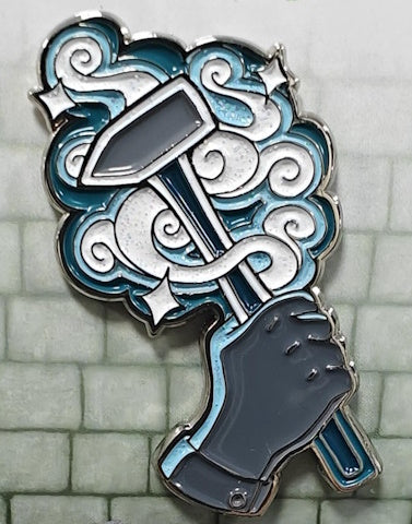 A glittering enamel pin featuring the Artificer character class with a design that includes teal, black, and grey colors, and a representation of a character's hand holding a smithy's hammer.