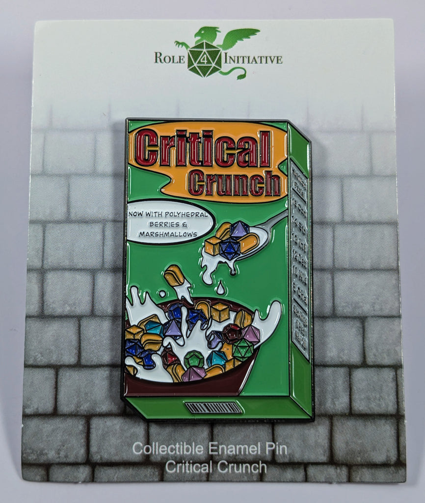 A colorful enamel pin depicting a box of Critical Crunch breakfast cereal with a spoon, now with berries and malted milk. Milk not included.