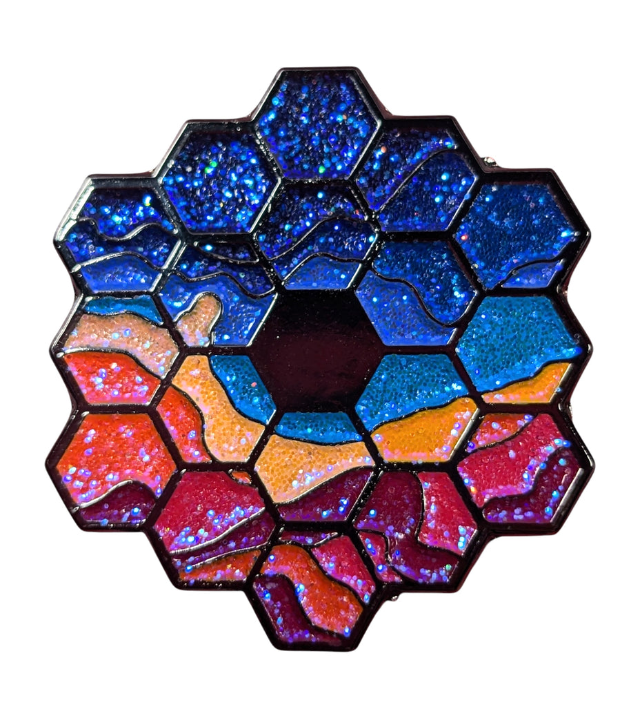 A collectible enamel pin with a multicolored, geometric patten based off the James Web Telescope with a glitter finish.